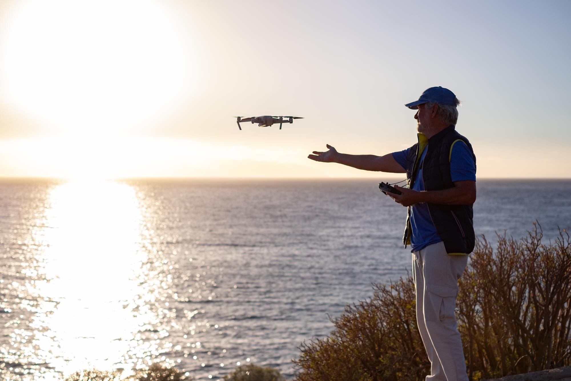 Senior man flying with drone at sunset using digit