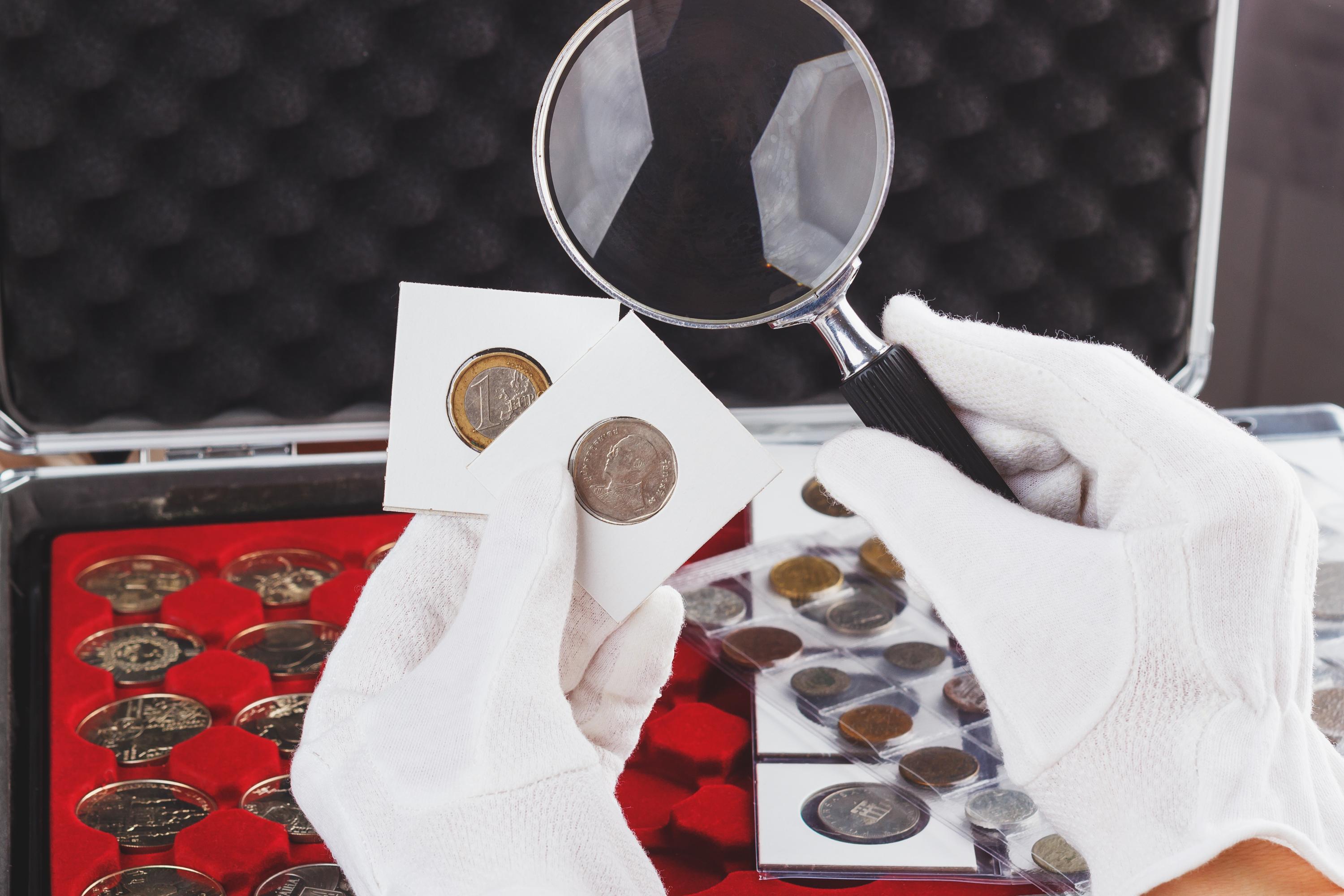Hands in the gloves hold magnifying glass and gold