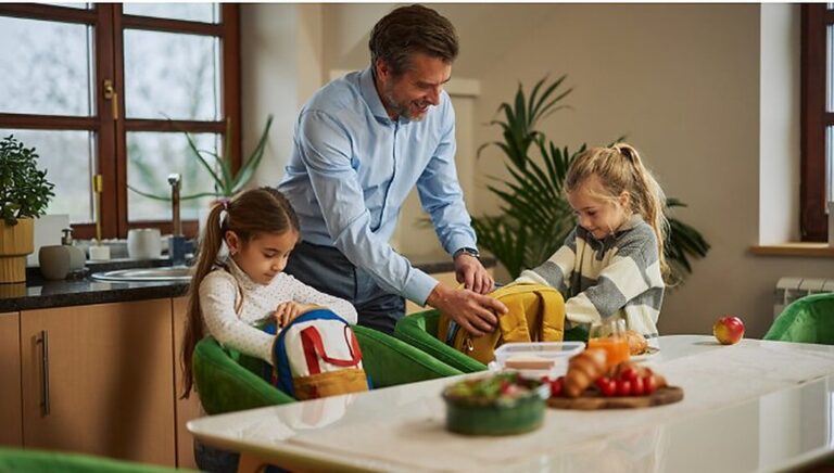 Father packing school lunches in a kitchen with his two children before the school day