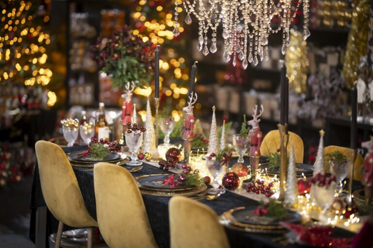 Festive holiday dinner table with gold chairs, candles, glassware, and string lights