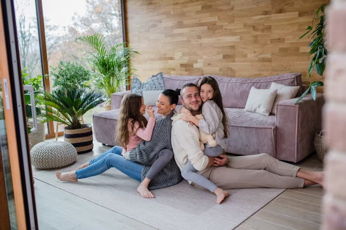 Family of four sitting together on a couch, smiling and relaxed, symbolizing the peace of mind that life insurance provides at every stage of life.